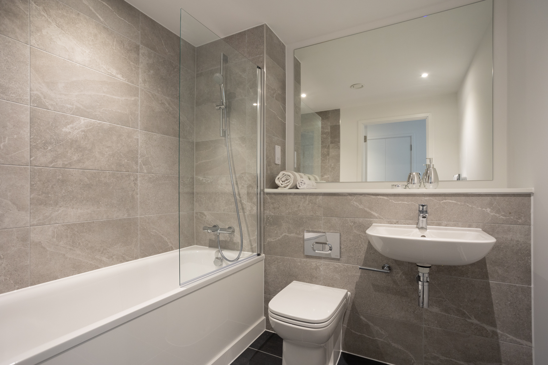 Interior view of bathroom white sink, bath and toilet, large glass mirror and grey marble tiles.