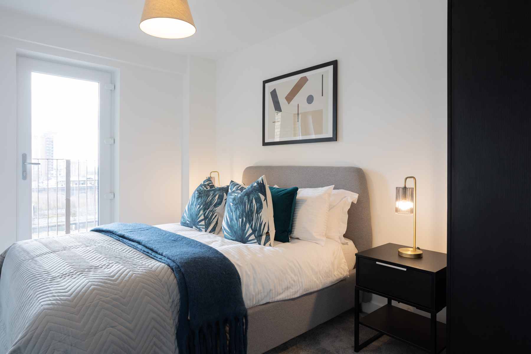 Bedroom with white walls, large grey bed with white and green pillows.