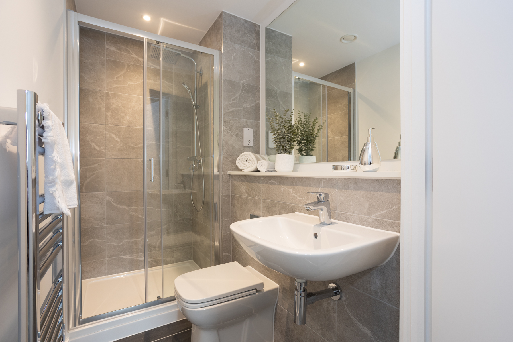 Interior view of bathroom white sink, shower and toilet, large glass mirror and grey marble tiles.