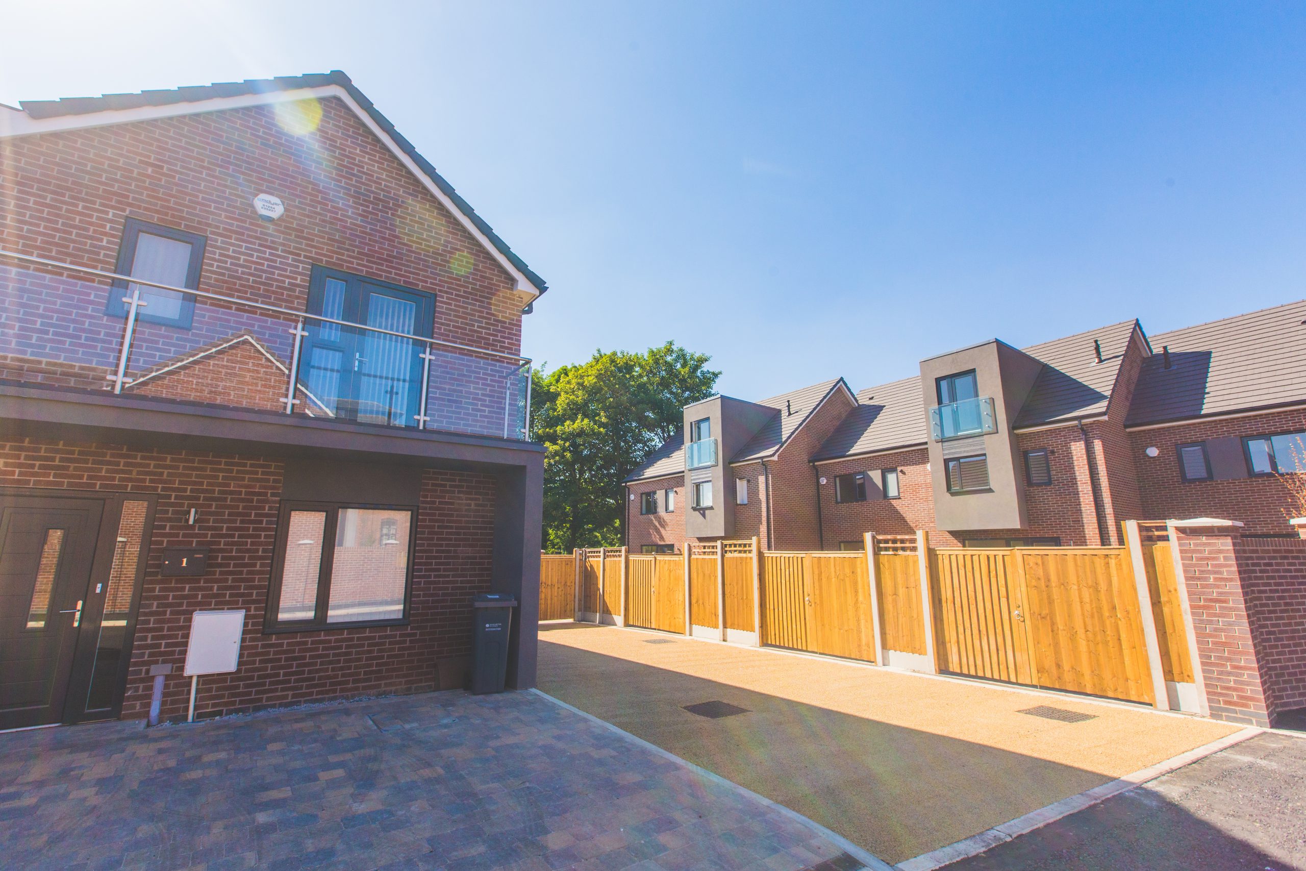 Close up view brick property with glass balustraded and block paving at the front. To the right is wooden fence then terraced houses.