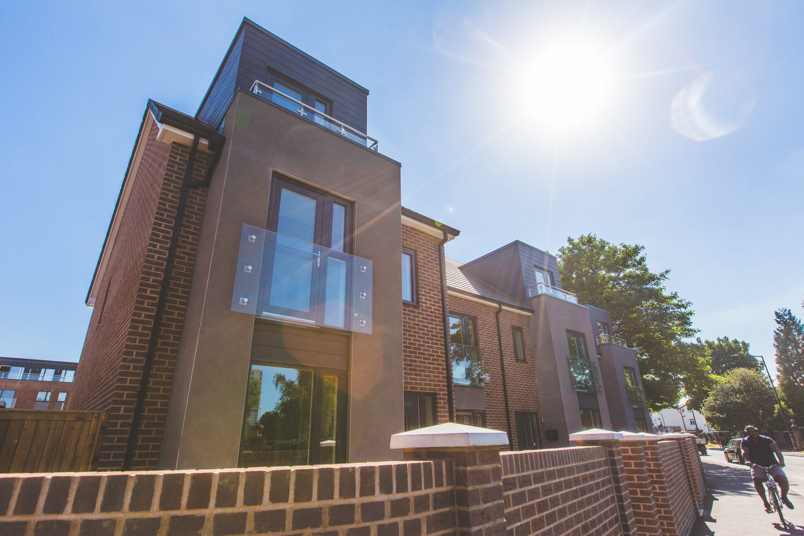 Close up view of large grey extension with glass balustrades and brick wall in front of property.