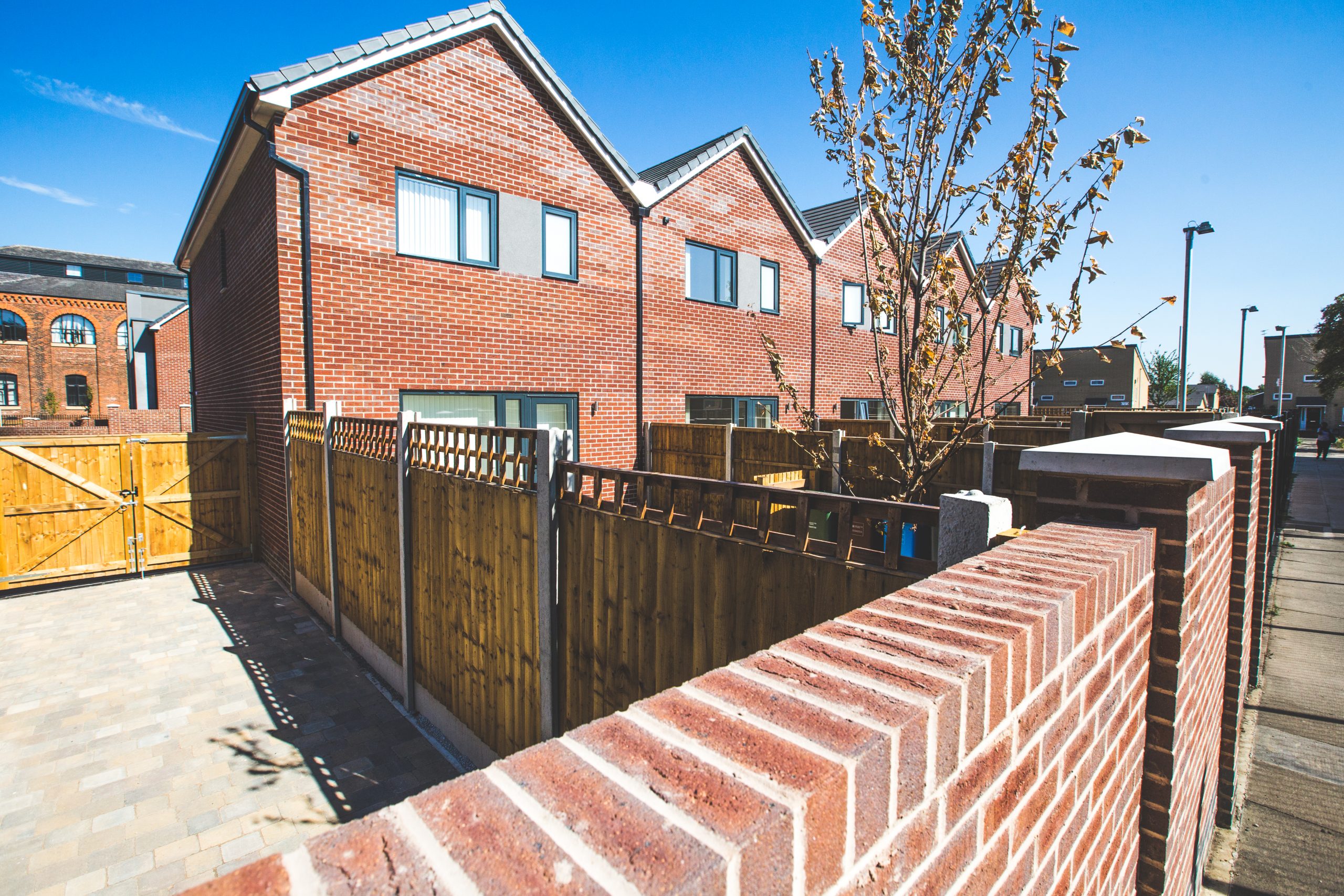 Street view looking over rear wall of 5 terraced properties, looking into grassed back gardens and divided by wooden fences.