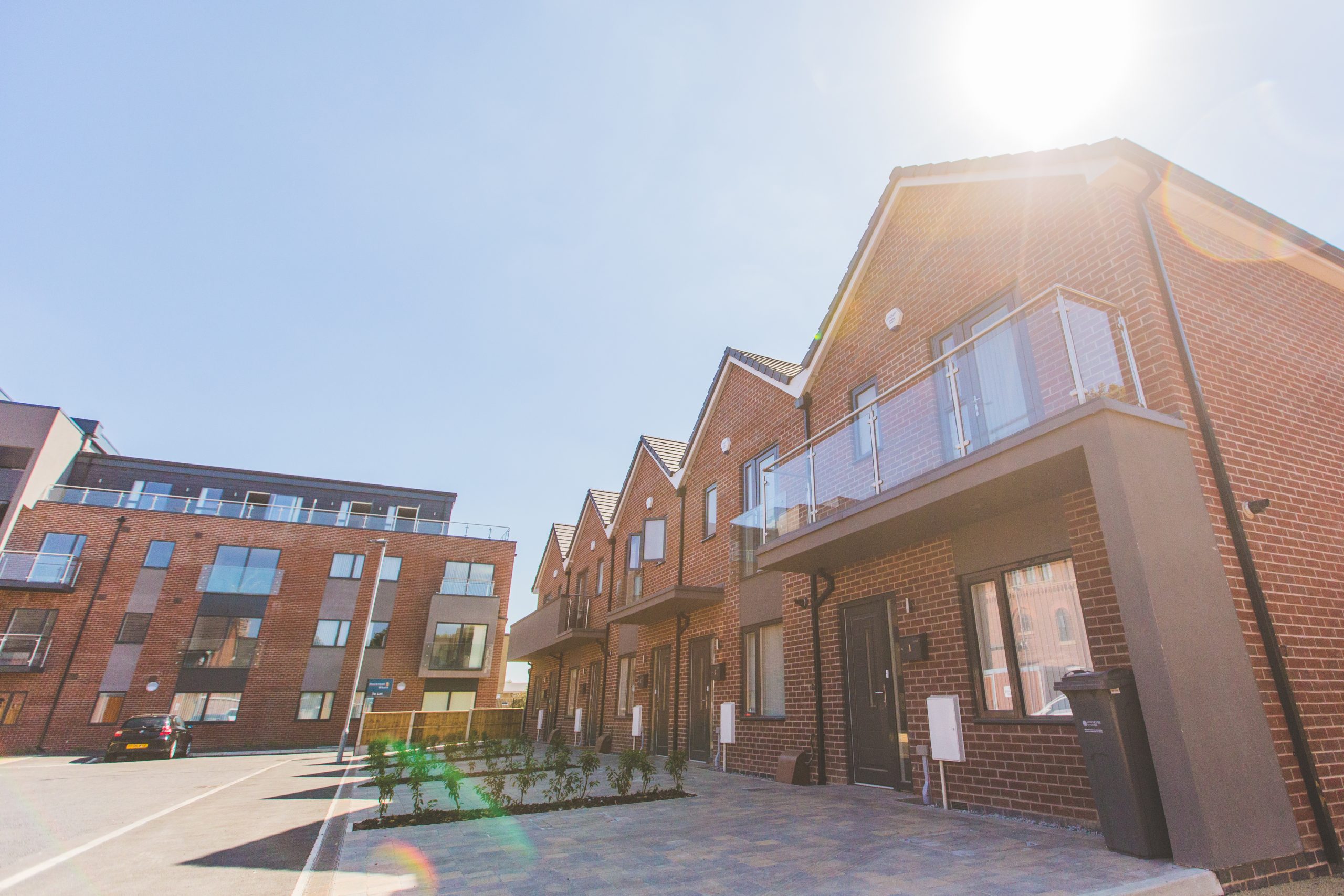 Five brick terraced houses on the right with some having glass balconies. In the distance is a five story apartment building.