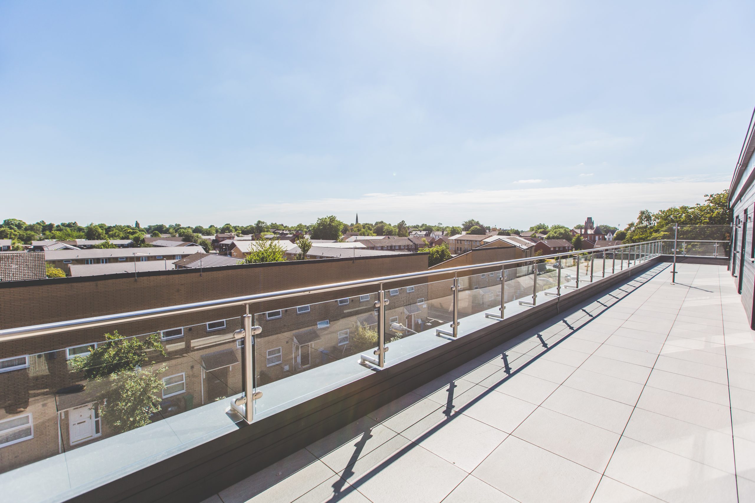 Exterior view from a large balcony with glass balustrade and bright blue sky.