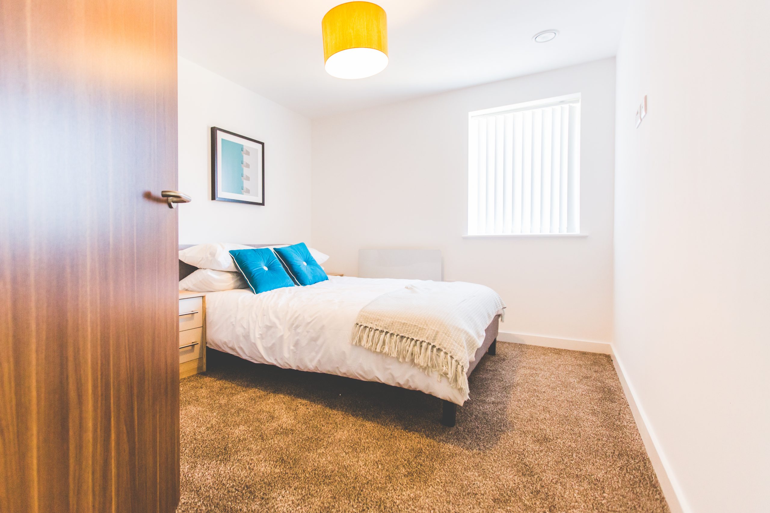 Bedroom with light brown carpet large bed with white sheets and green pillows.