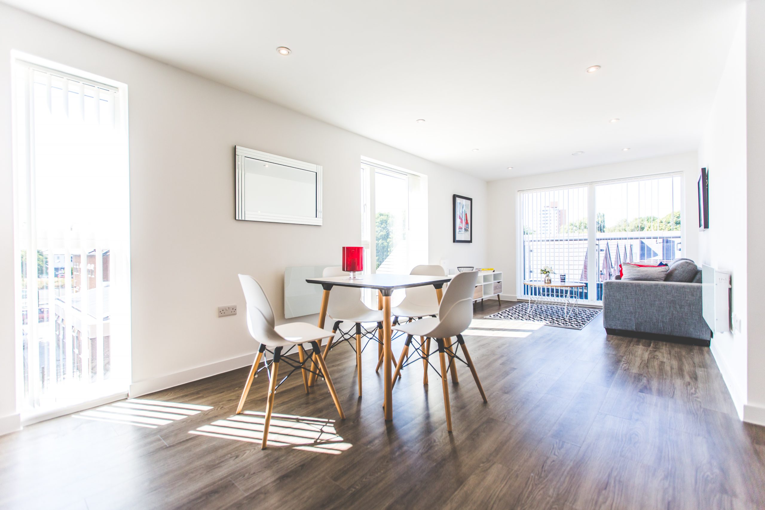 Large apartment with dark wooden floor white table and chairs with a sofa in the background.