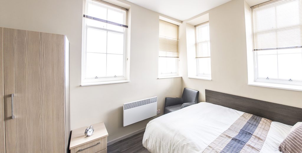 View of double bed and three bright windows.