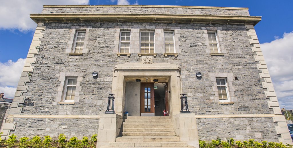 Large building with grey brick and stone steps leading up to the entrance.