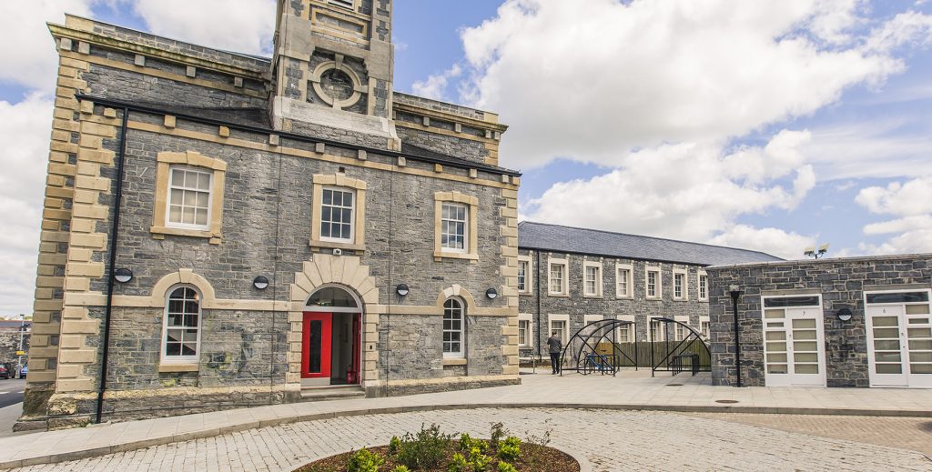 Exterior front view of the court house, with grey stone and a small tower in the center of the roof.