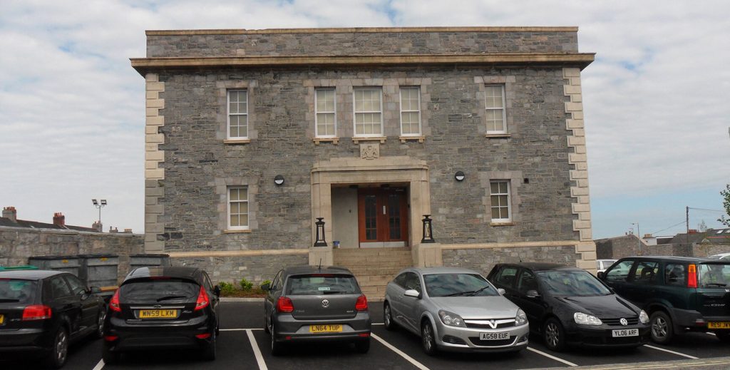 Vie of the car park at the Court House with a large grey brick building behind.