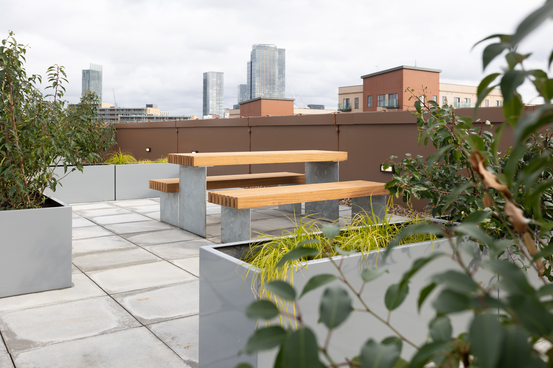 Rooftop view with picnic bench and large grey planters with green shrubs.