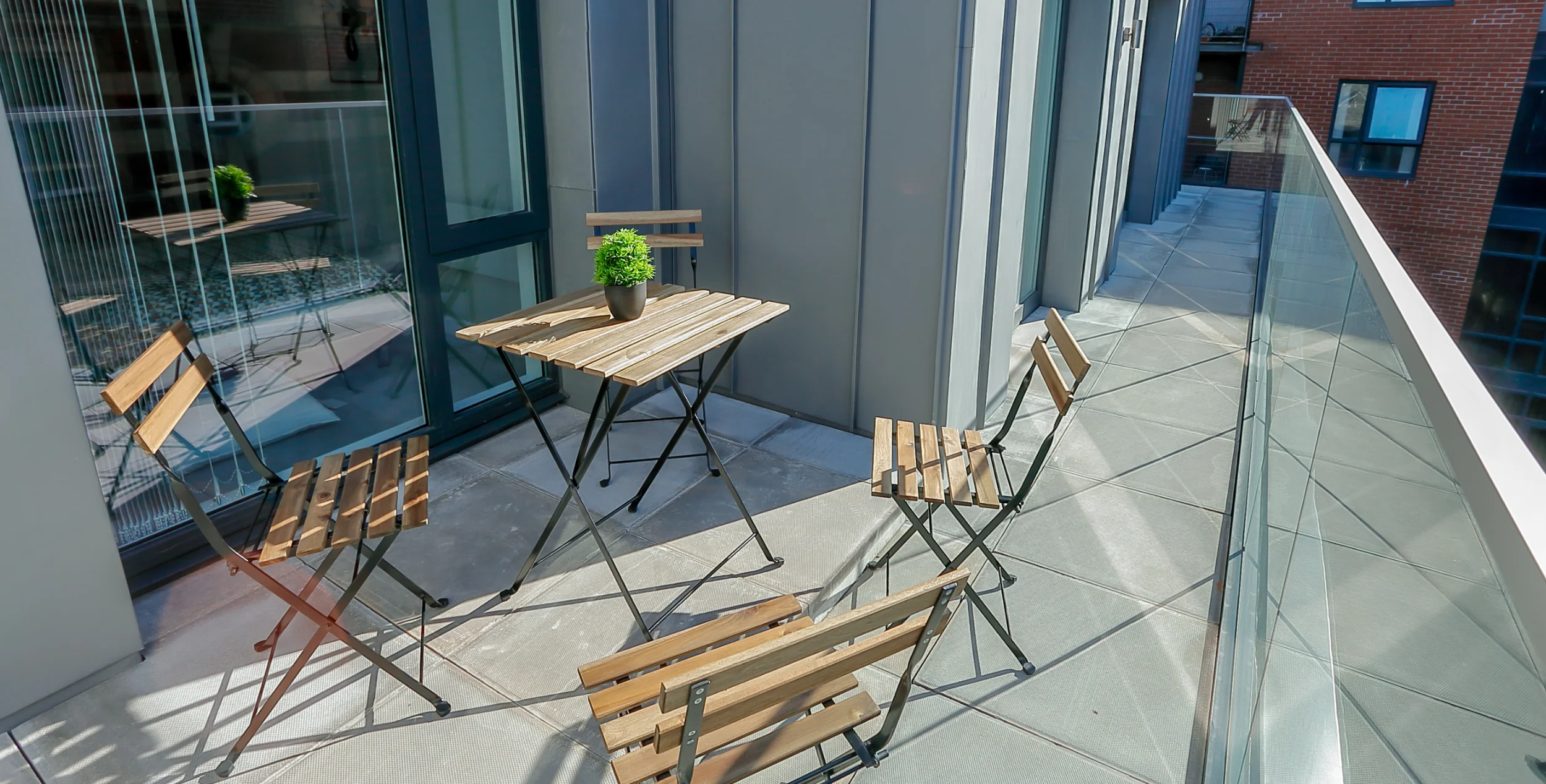Long balcony with glass balustrade and small wooden table and chairs.