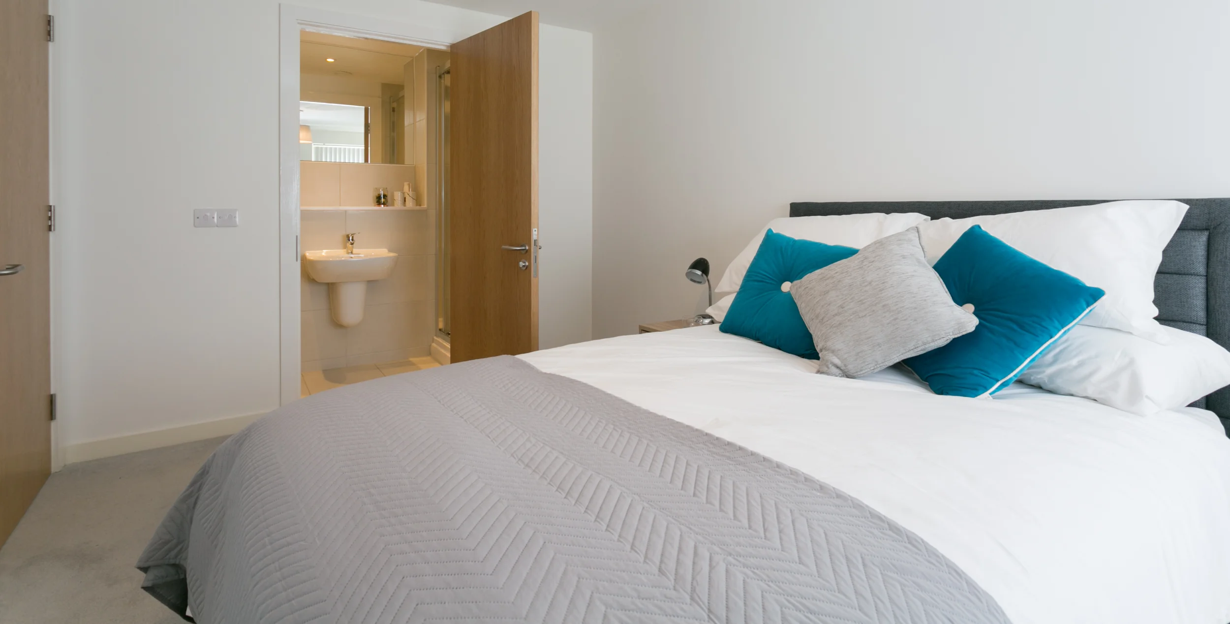 View looking over a modern double bed with an ensuite in the background along site the bed.