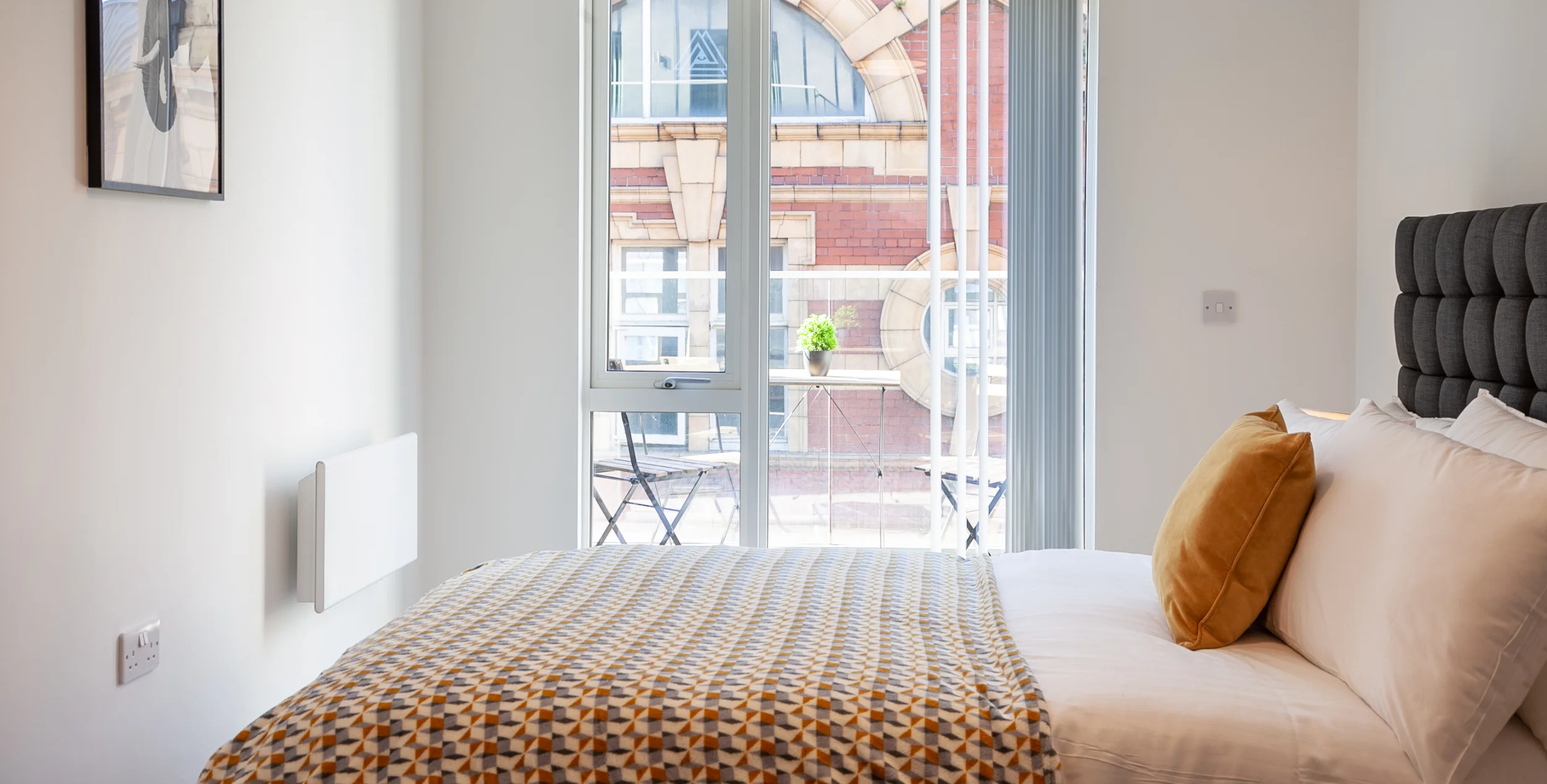 View looking over a modern double bed with a glass window and door leading onto a balcony.