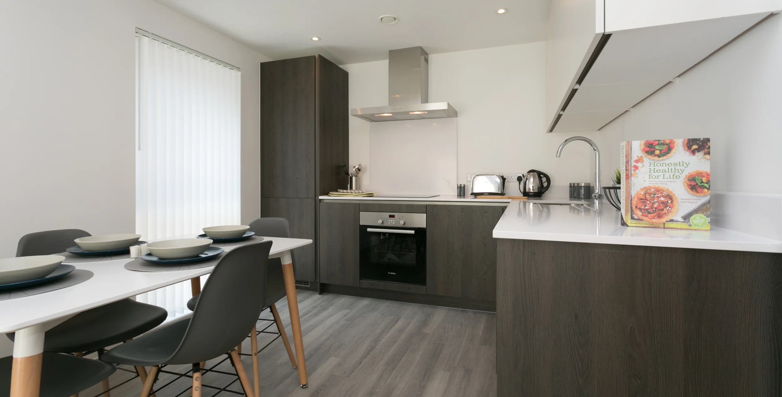 Kitchen diner with dark brown kitchen doors and dining table in front.