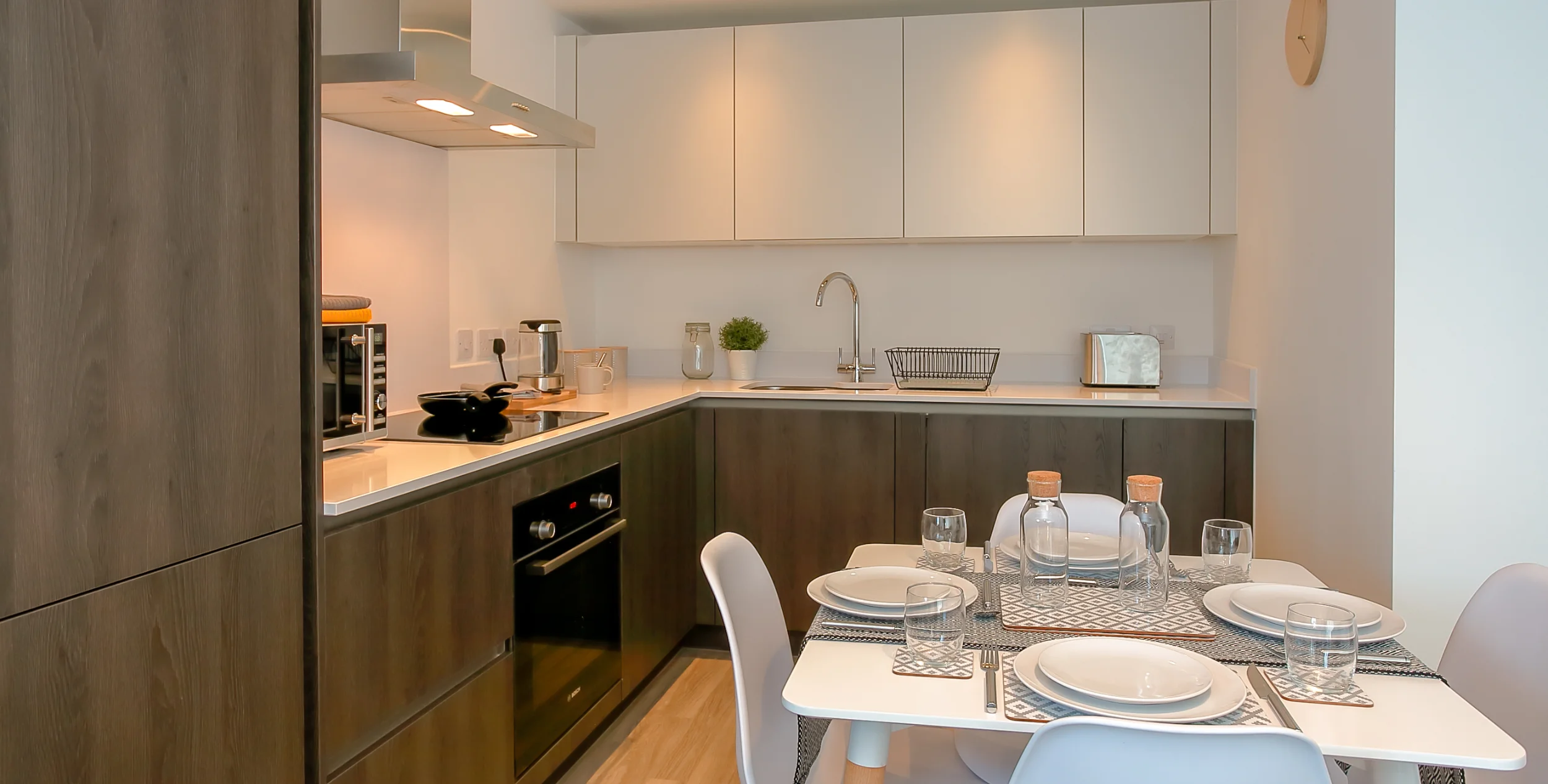 Lighter coloured wooden kitcken units with a dining table in font.
