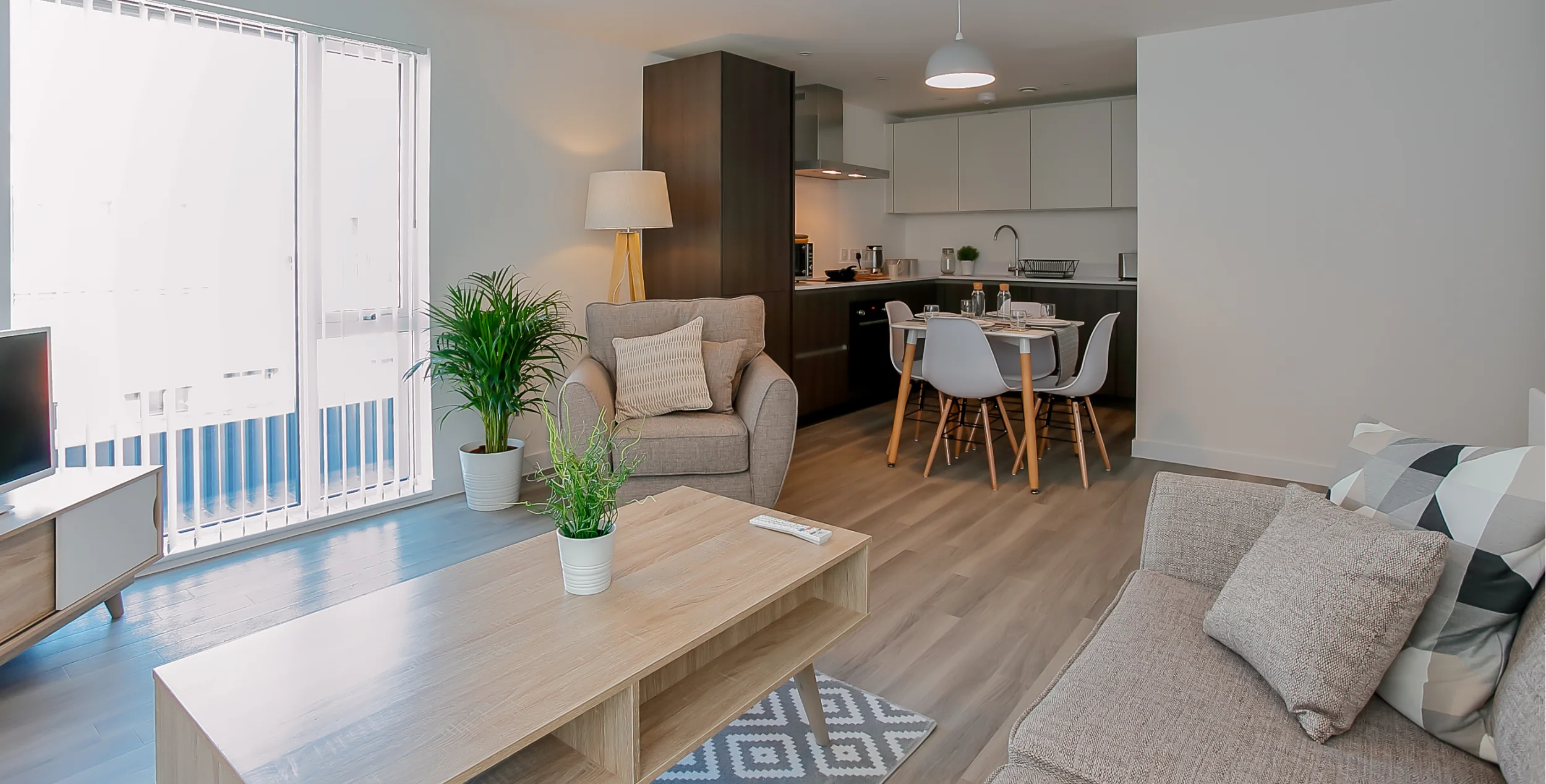 Large kitchen diner and lounge, showing kitchen in the forground, with dining table in front and then a light coloured three piece sofa with a light wooden floor.