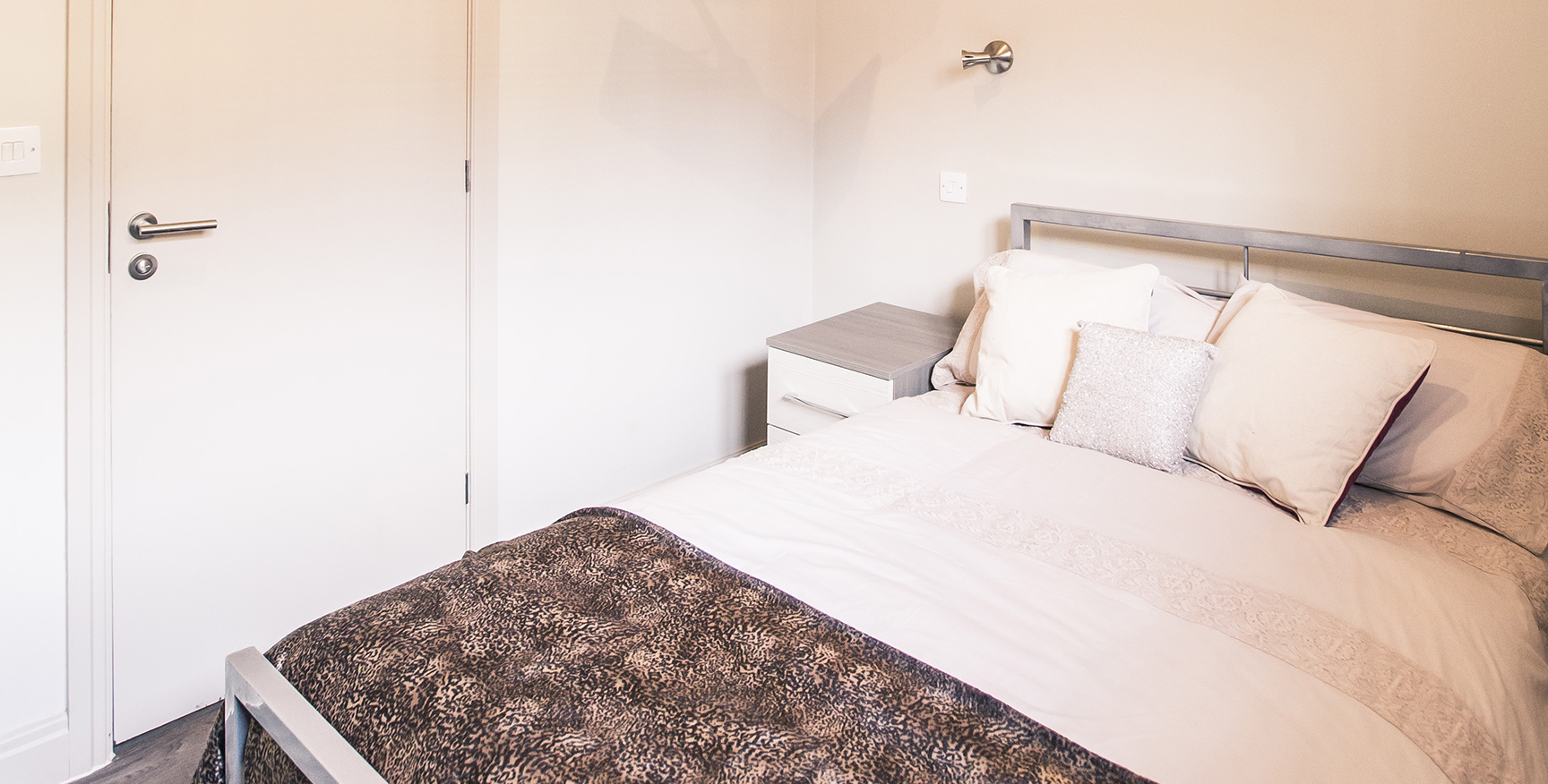 Double bed with silver metal bed frame, with white pillows and sheets with a brown throw.