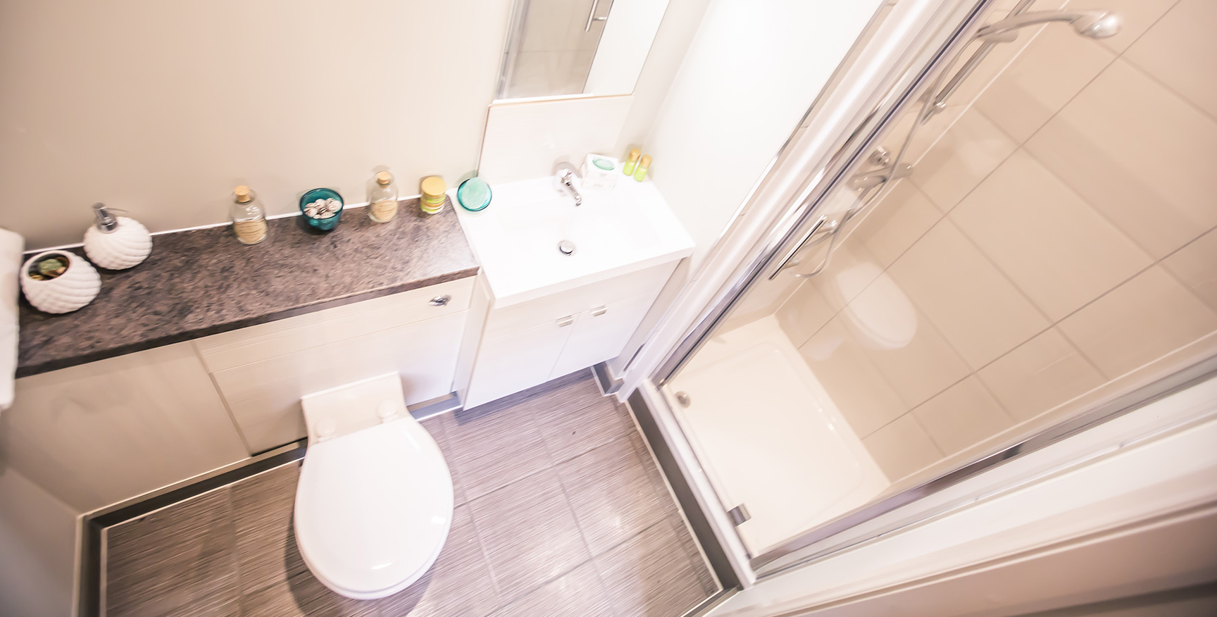 Looking directly down from the ceiling at a bathroom with a grey tiled floor, a white sink, a white toilet and a shower cubicle.