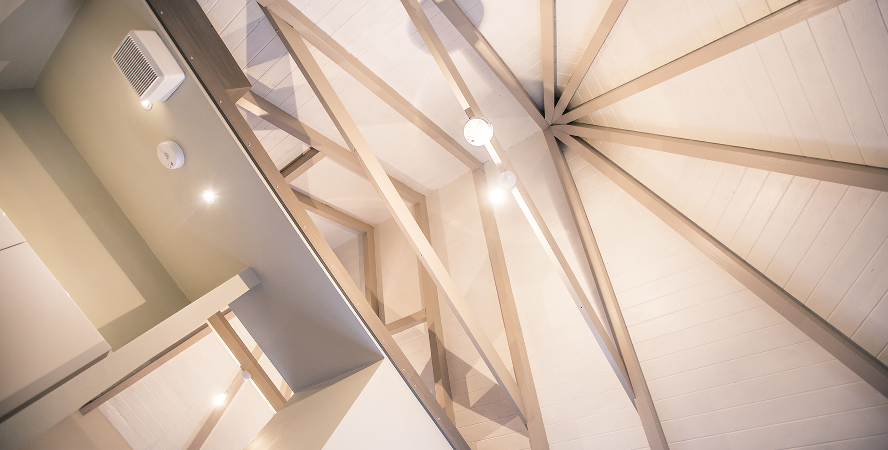 Looking directly up at a vaulted ceiling with wooden beams.