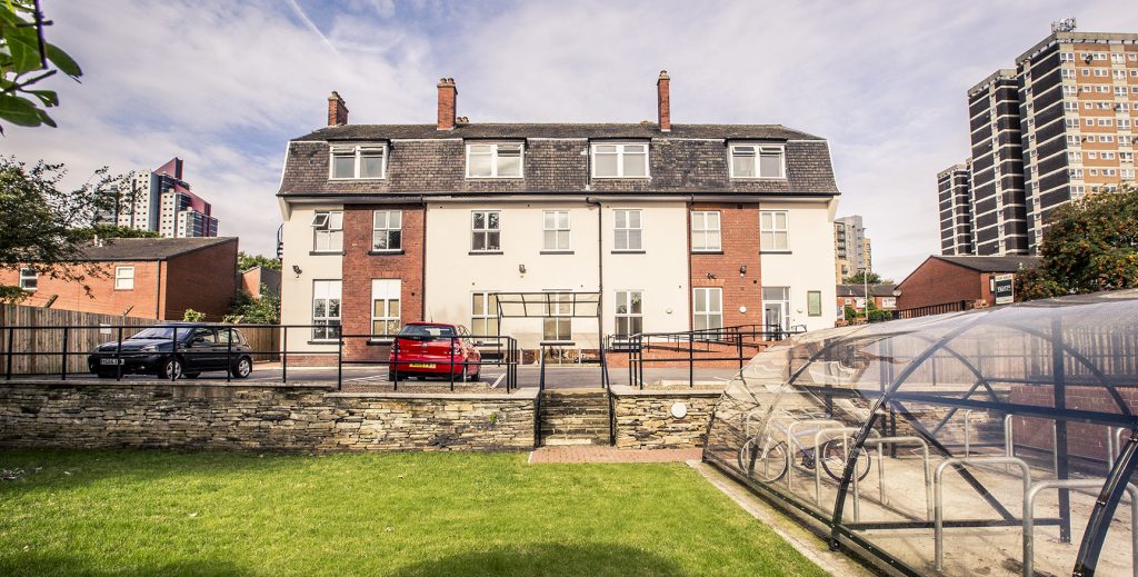 Exterior view of Lovell Park student accommodation, with covered parking for bicycles, an open grass area and parking for students.