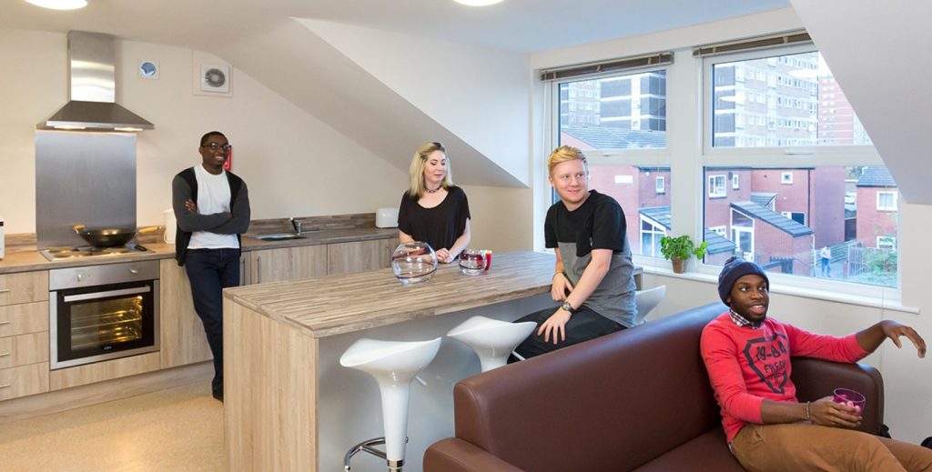 Modern open plan kitchen diner with four students talking and watching the TV.