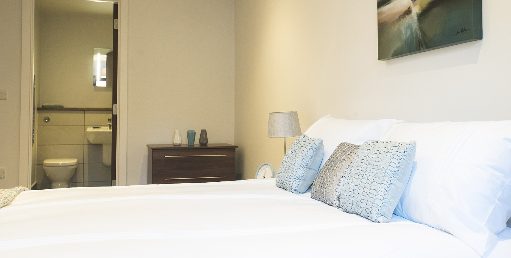 Side view of a white double bed with an en-suite in the background.