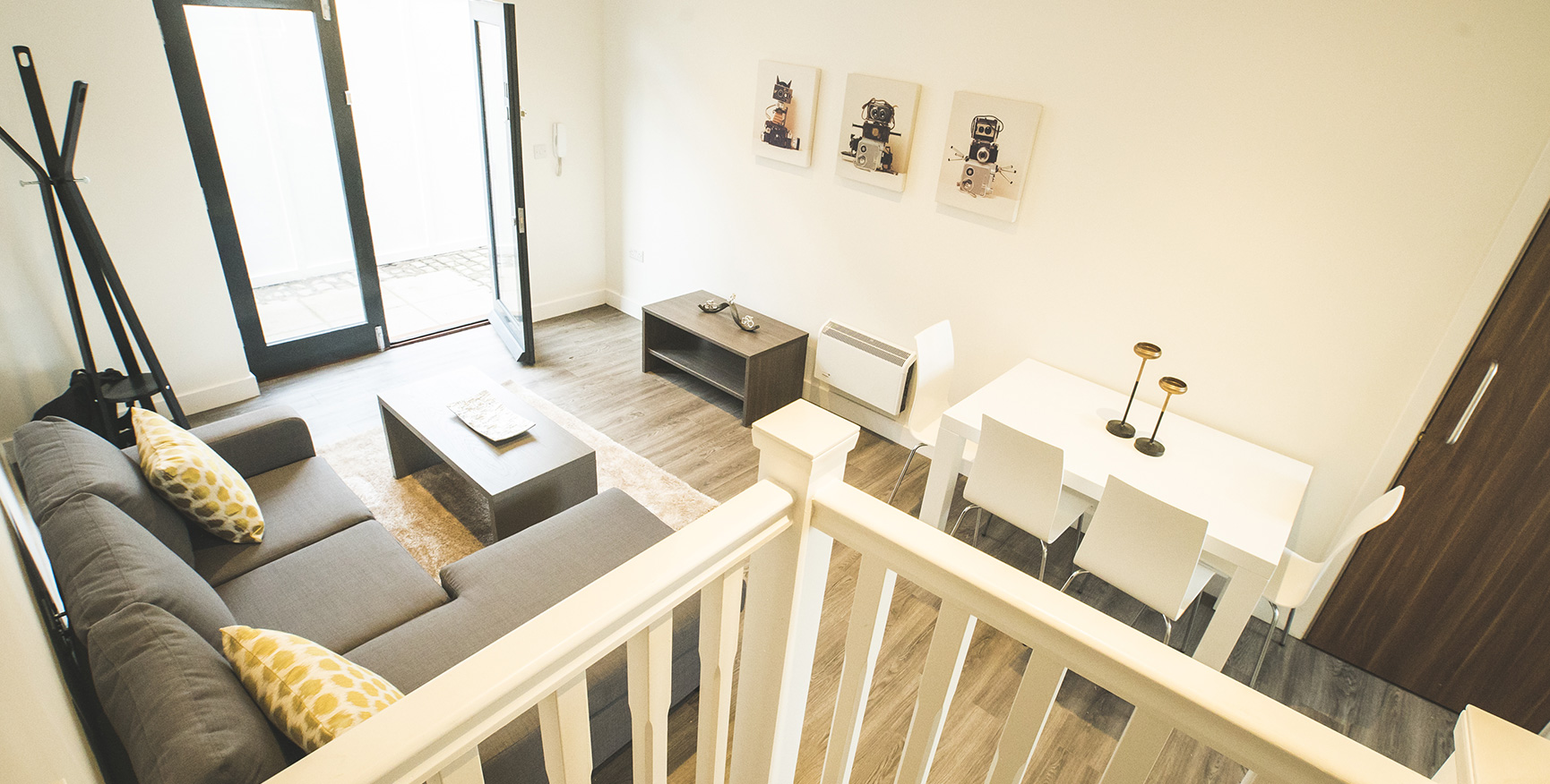 Elevated view looking down at an apartment with a dark sofa, white walls, wooden floors and white table and chairs.