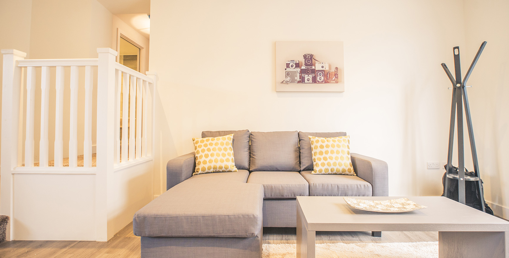 Level view of a grey three seated sofa in an apartment with a light coffee table in front and white bright walls.