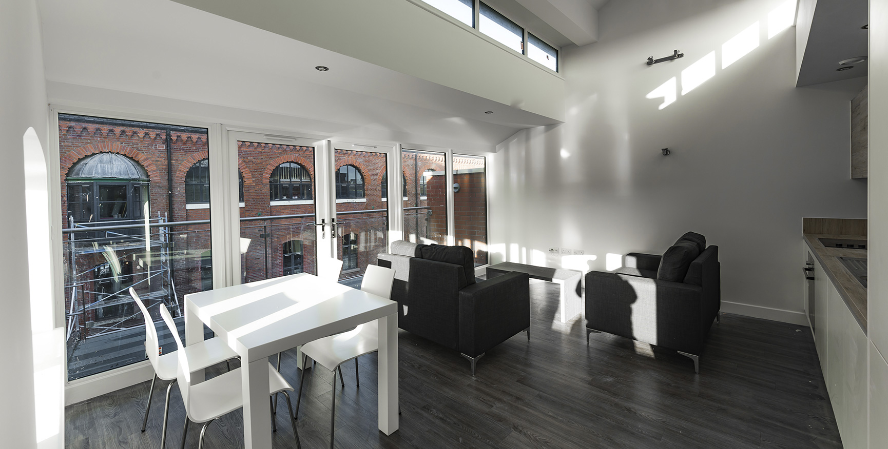 Interior view of Queens Brewery apartment with a large open window, dark wood floors, white walls and white table and chairs.