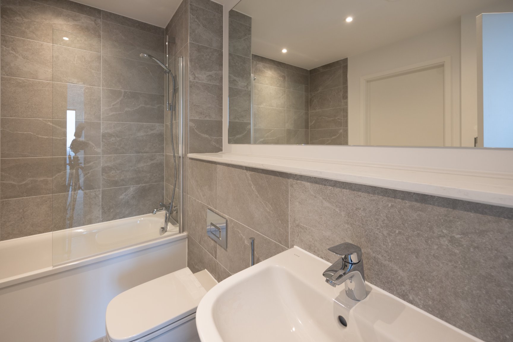 Silkbank Wharf bathroom with light grey marble tiles, large mirror and white sink, toilet and bath.