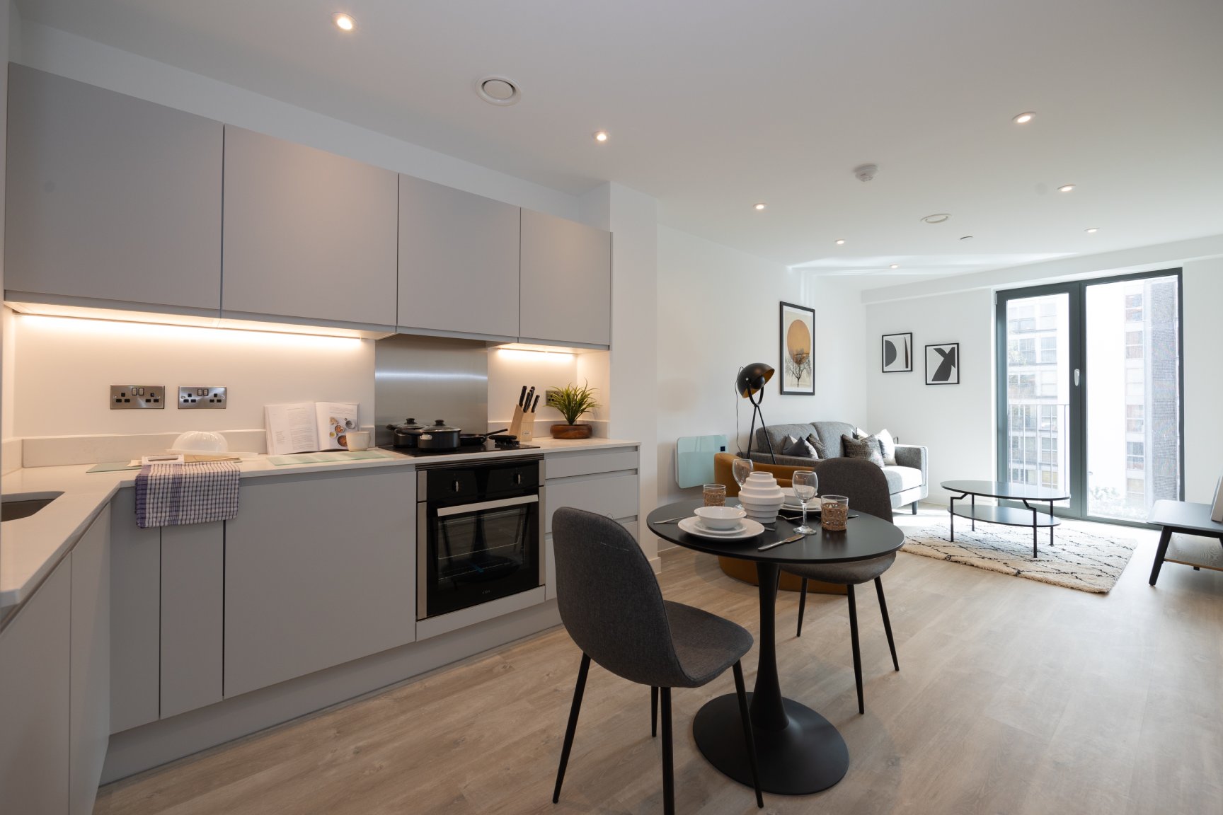 Large open plan apartment with a white kitchen, grey table and chairs, sofa and coffee table in the background.