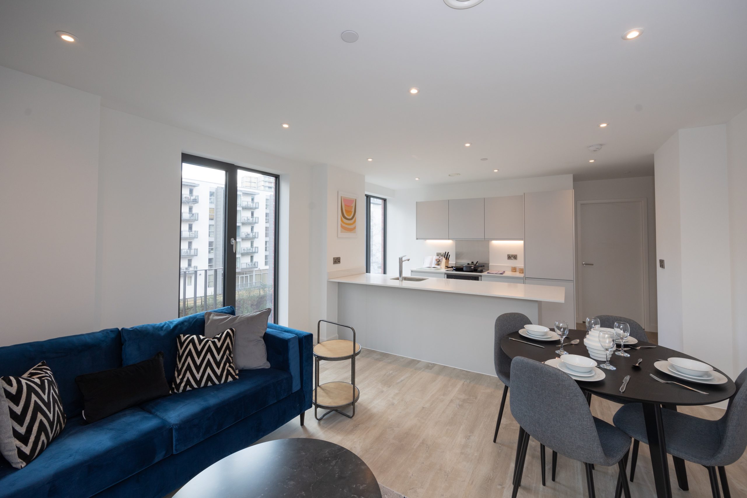 Modern open plan apartment with a blue sofa, grey table and chairs and white kitchen.