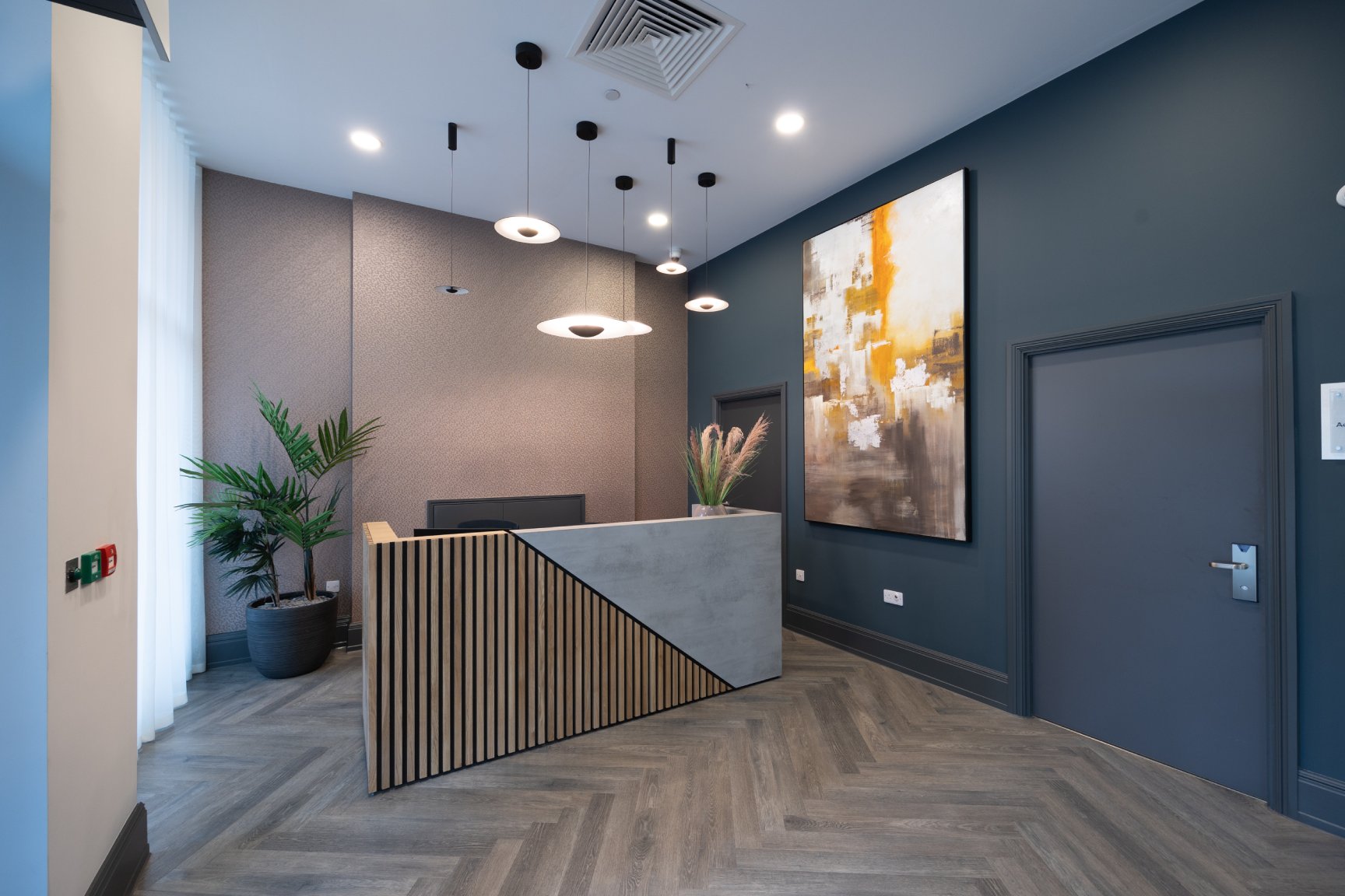 Reception area with wooden floors reception desk and large contemporary picture on the wall.