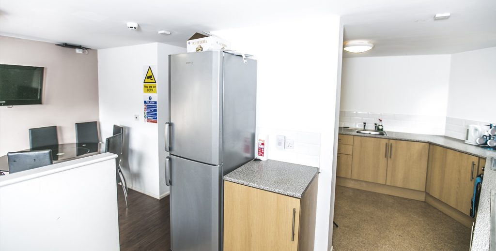 Communal kitchen with dining table and chairs, fridge freezer and wooded kitchen units.