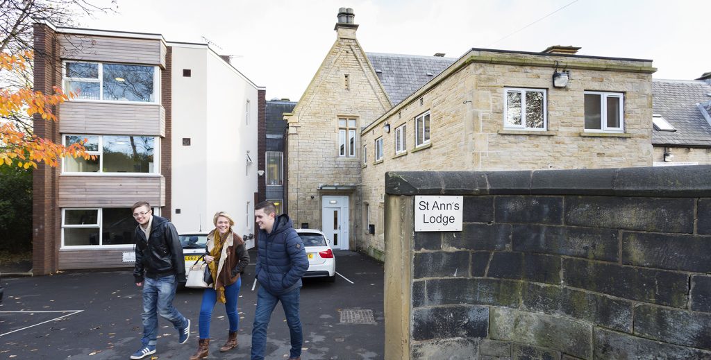 Three students walking out of the tall stone wall entrance.