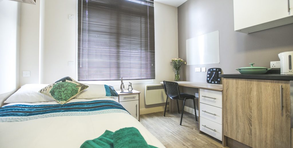 View of bed desk and kitchen in room