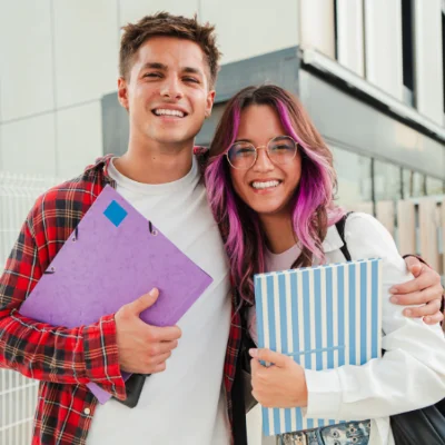 Two students with folders under their arms smiling directly at the camera.