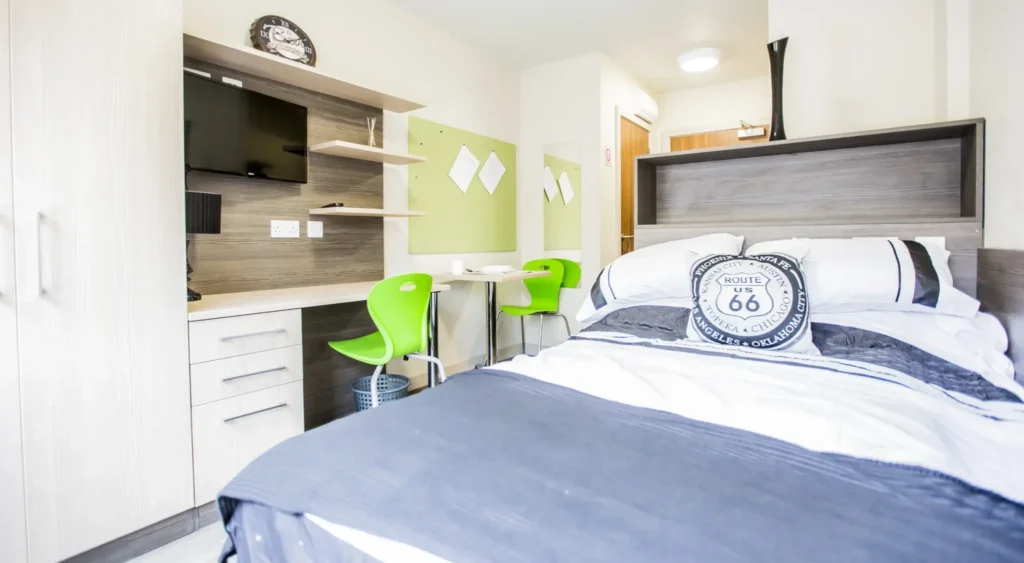 Student room with study area and TV on wall.